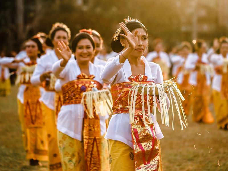 Beyaz sarı geleneksel kıyafetleri ile arka arkaya dizilmiş el sallayan Bali'li kızlar